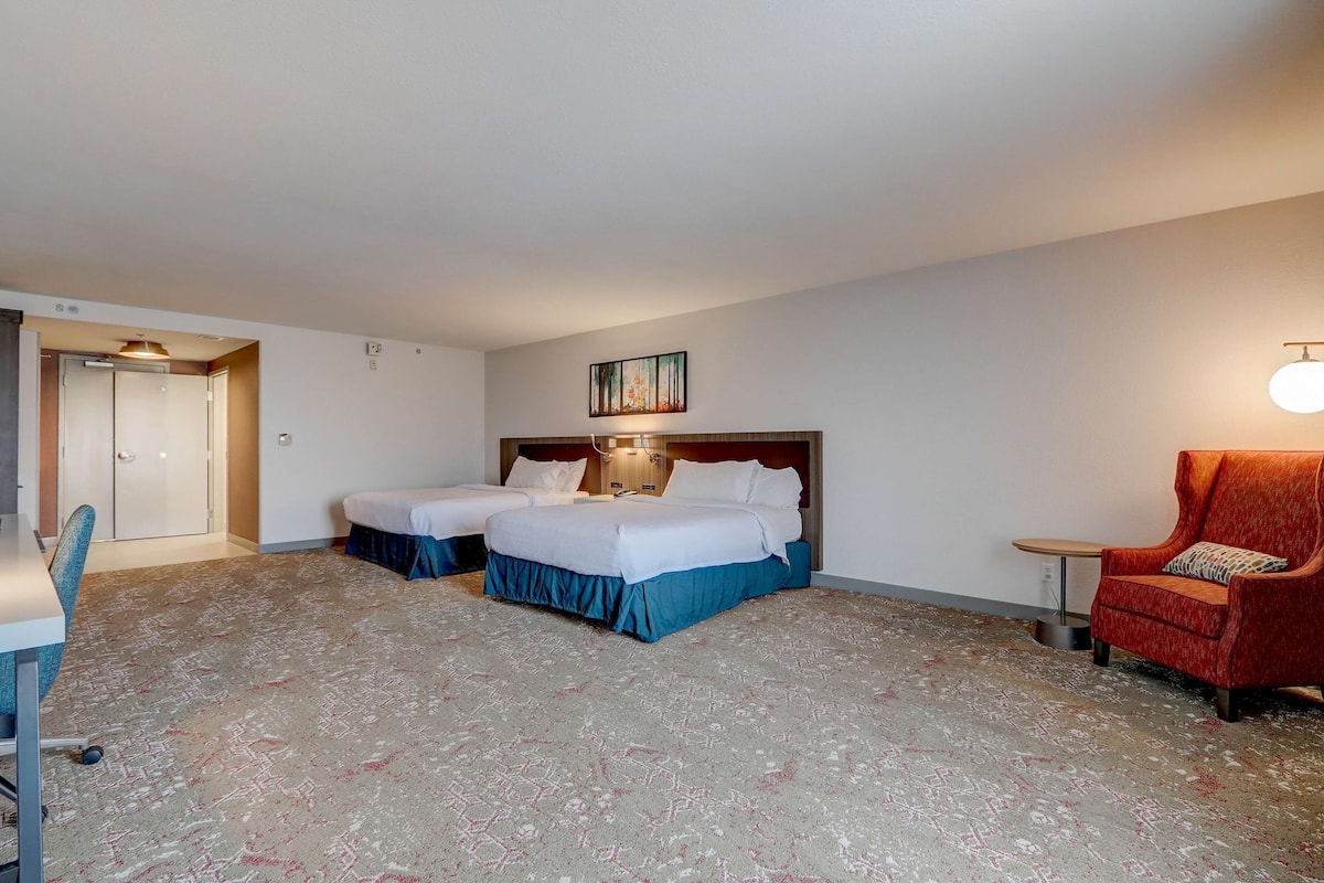 A hotel room with two beds, a desk, a chair, and a small table.