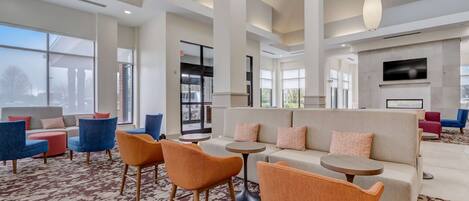 A spacious lobby with a large seating area, a fireplace, and large windows offering a view of the outside.