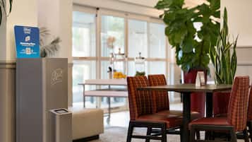 Habitación de hotel con minibar, comedor con mesa y sillas, y una planta grande en maceta.