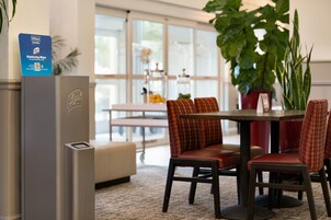 A hotel room with a minibar, a dining area with a table and chairs, and a large potted plant.