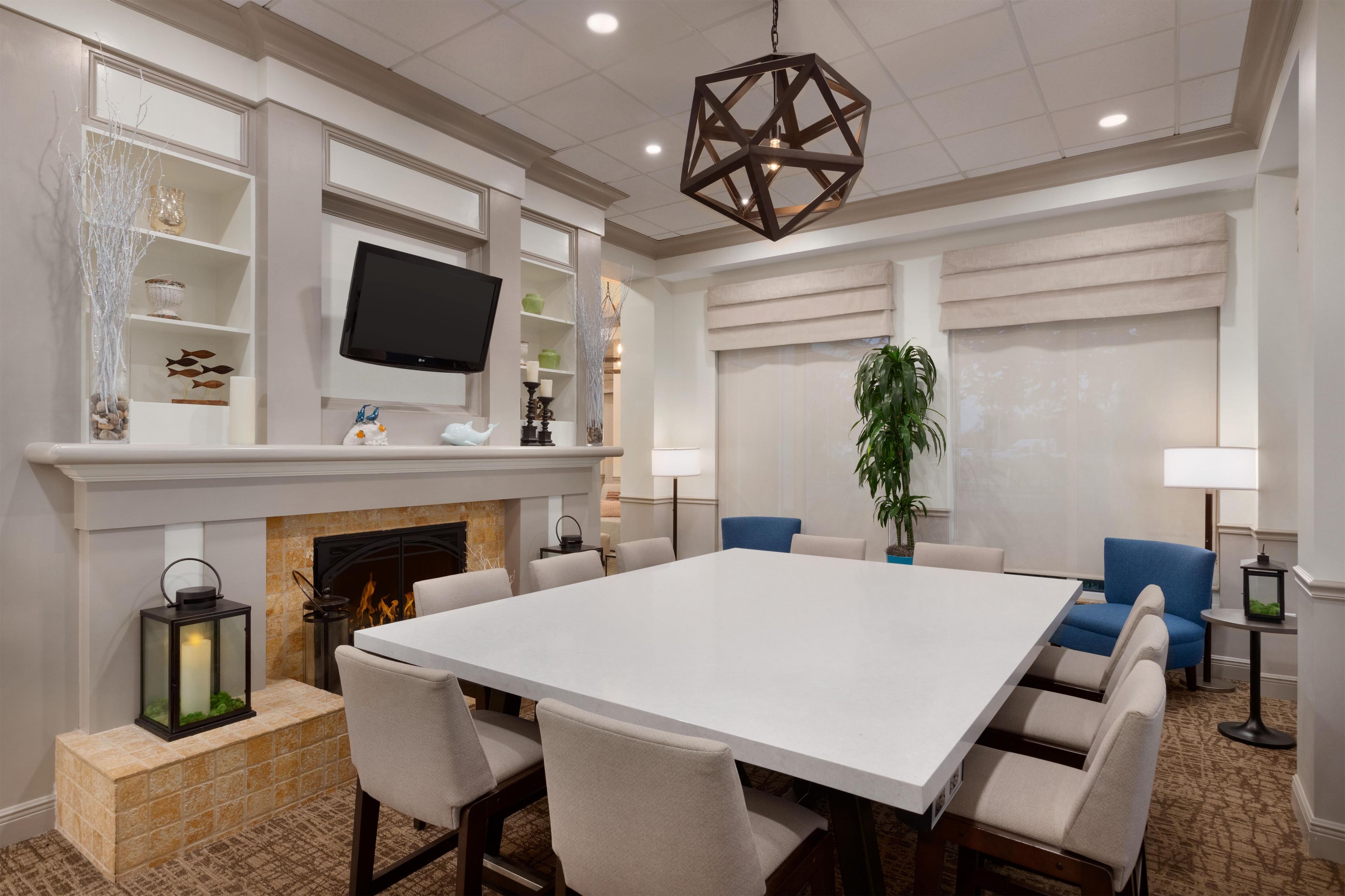 A spacious room with a large white table, comfortable seating, a fireplace, a television, and a decorative hanging light fixture.