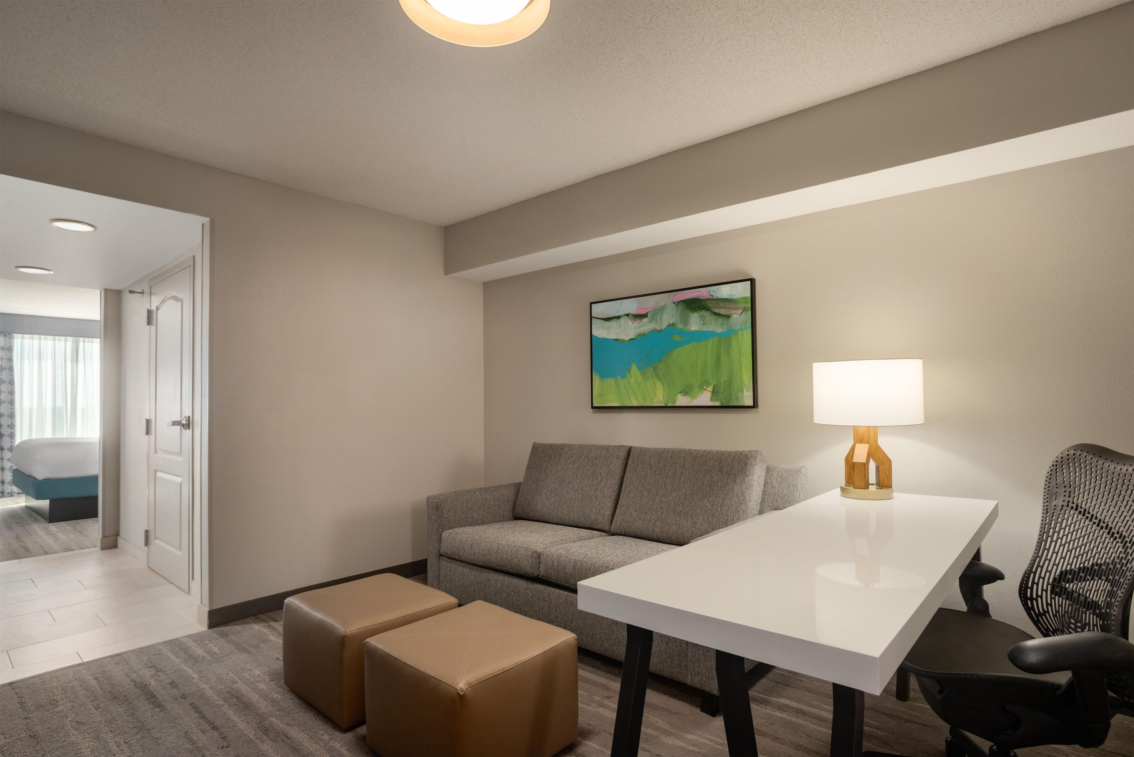 A hotel room with a gray sofa, a white table, and a painting on the wall.