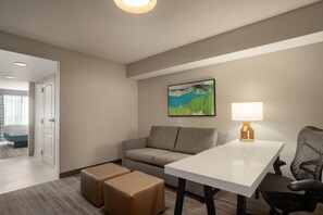 Una habitación de hotel con un sofá gris, una mesa blanca y un cuadro en la pared.