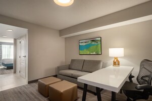 A hotel room with a gray sofa, a white table, and a painting on the wall.