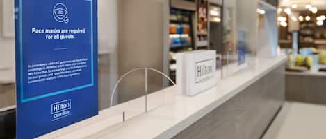 Una zona de recepción de hotel limpia y moderna, con un letrero azul que indica que se requiere el uso de mascarillas para todos los huéspedes.