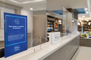 A clean, modern hotel reception area with a blue sign indicating face masks are required for all guests.