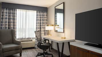 A hotel room with a desk, chair, air conditioning unit, and a television.