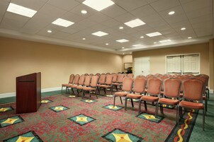 A conference room with rows of chairs, a podium, and a patterned carpet.