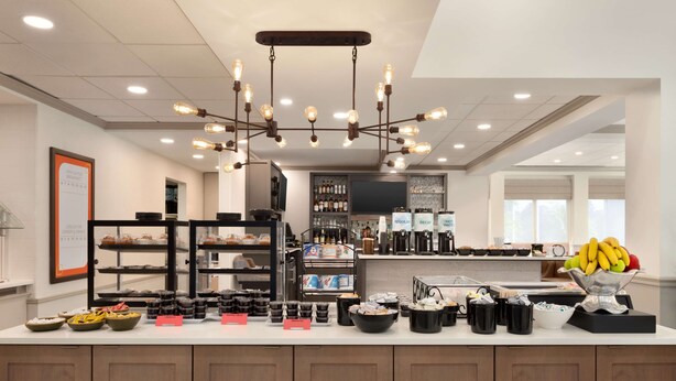 A breakfast bar with various food items and beverages, a coffee station, and a fruit bowl.