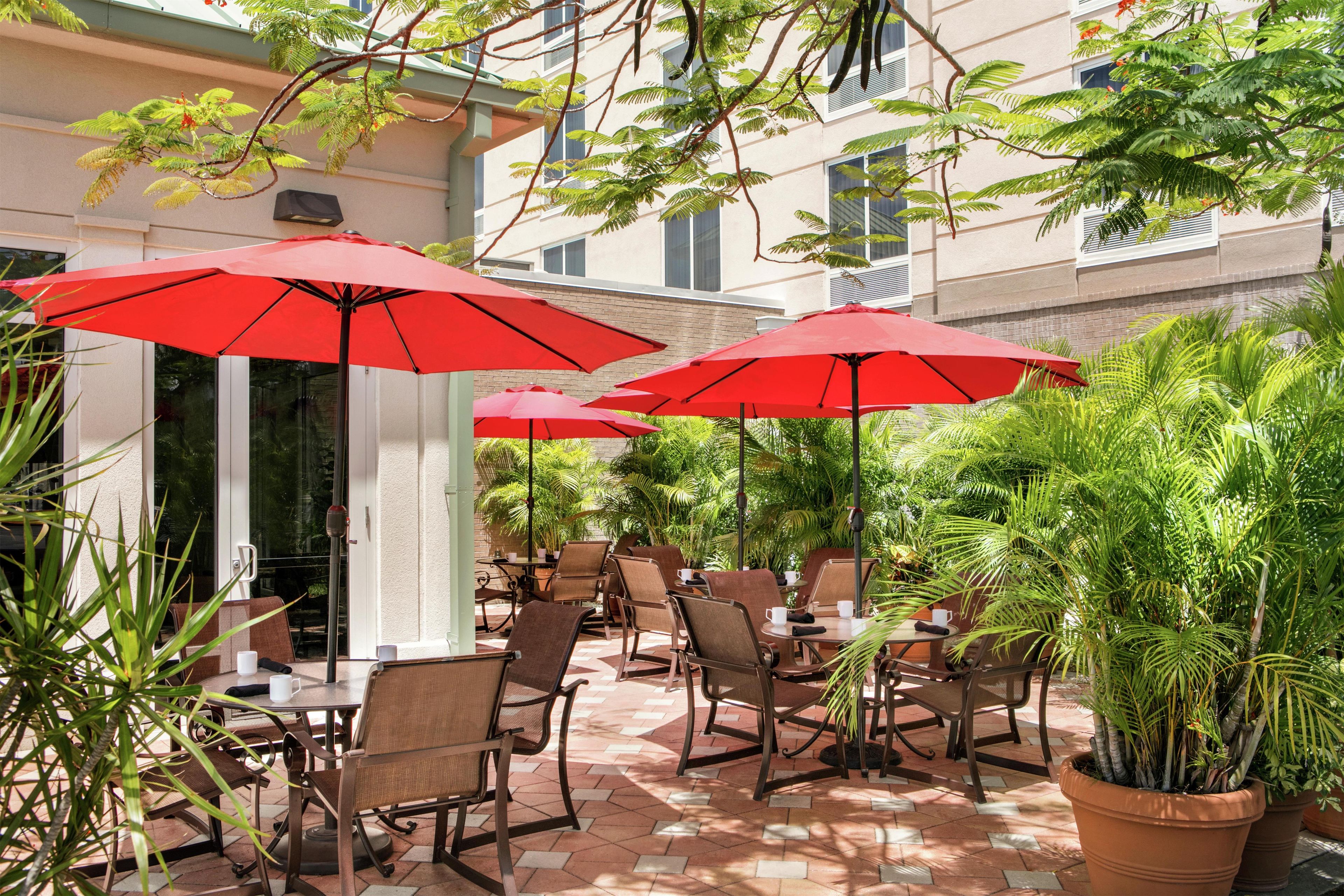 Un espace extérieur aménagé en terrasse, avec des parasols rouges, des chaises en osier et des plantes en pot.