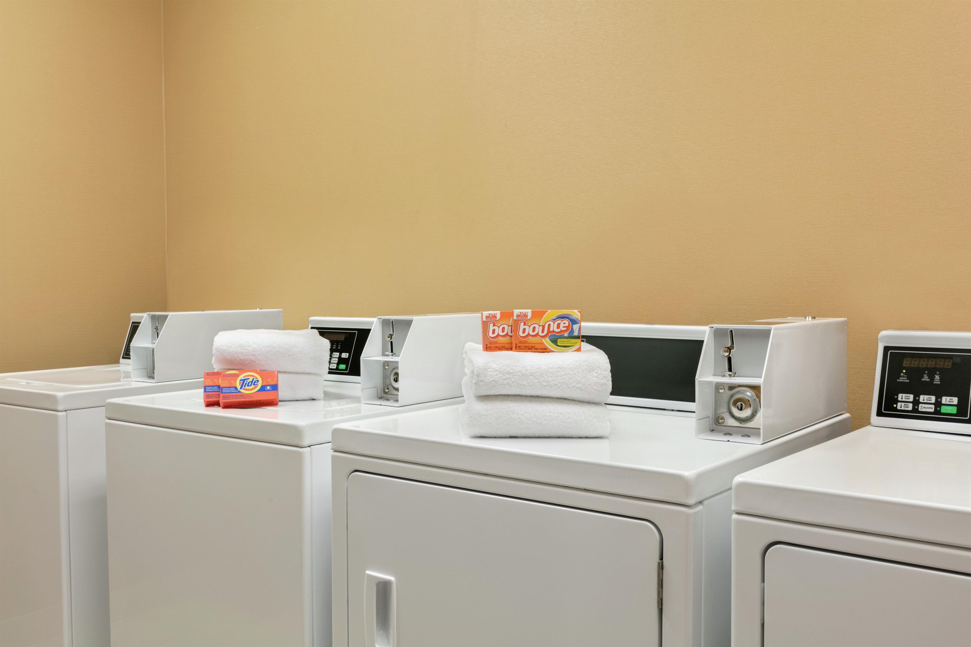 A laundry area with multiple washing machines, a control panel, and Tide detergent boxes.