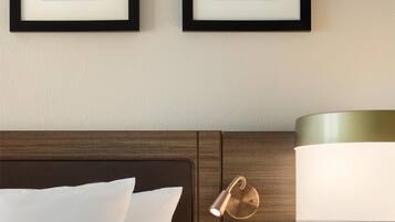 A neatly made bed with white linens, a wooden headboard, and a bedside table with a lamp. Two framed artworks are hung on the wall above the bed.