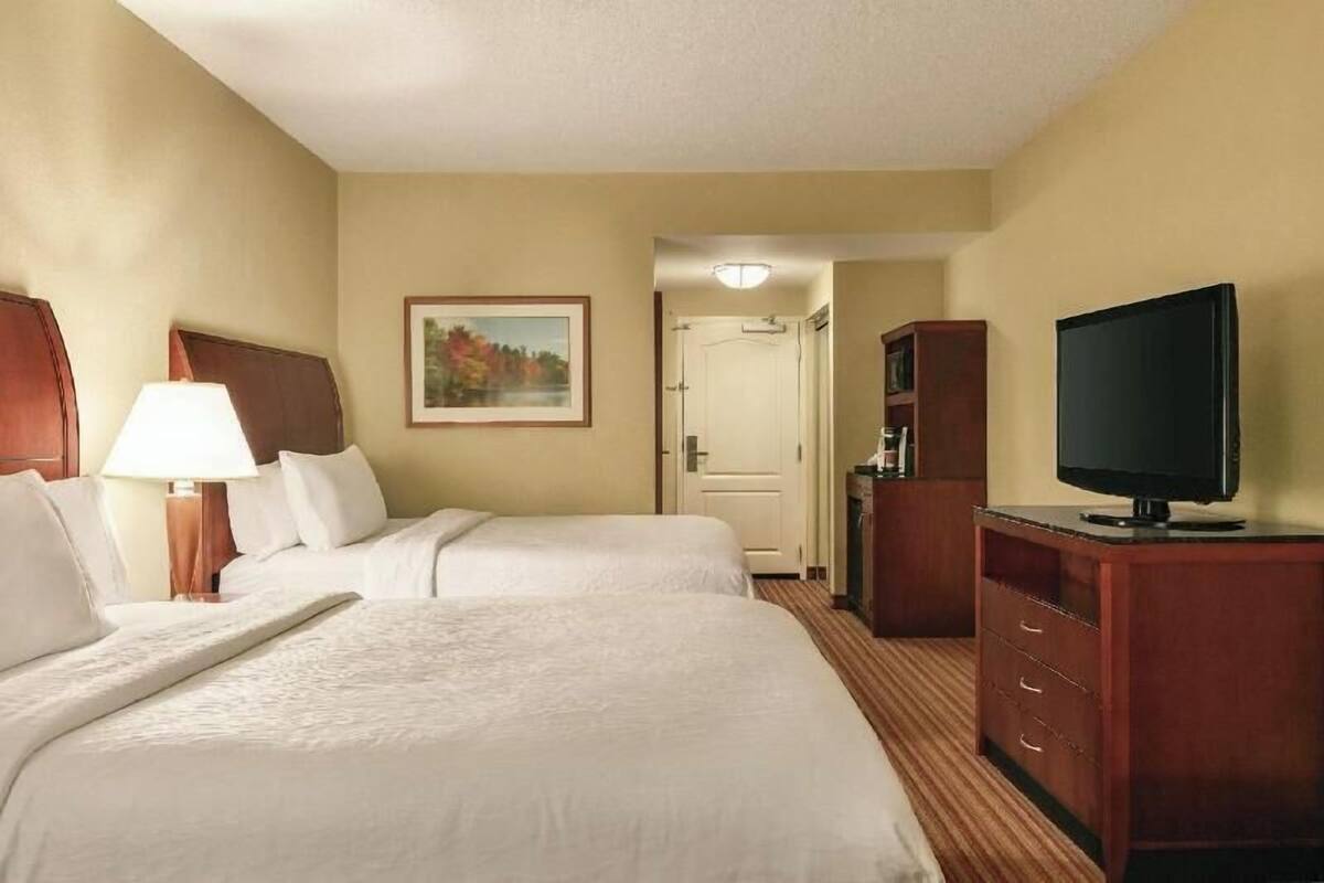 Hotelkamer met twee bedden, een televisie, een bureau met een lamp, een schilderij aan de muur en een deur naar een andere kamer.