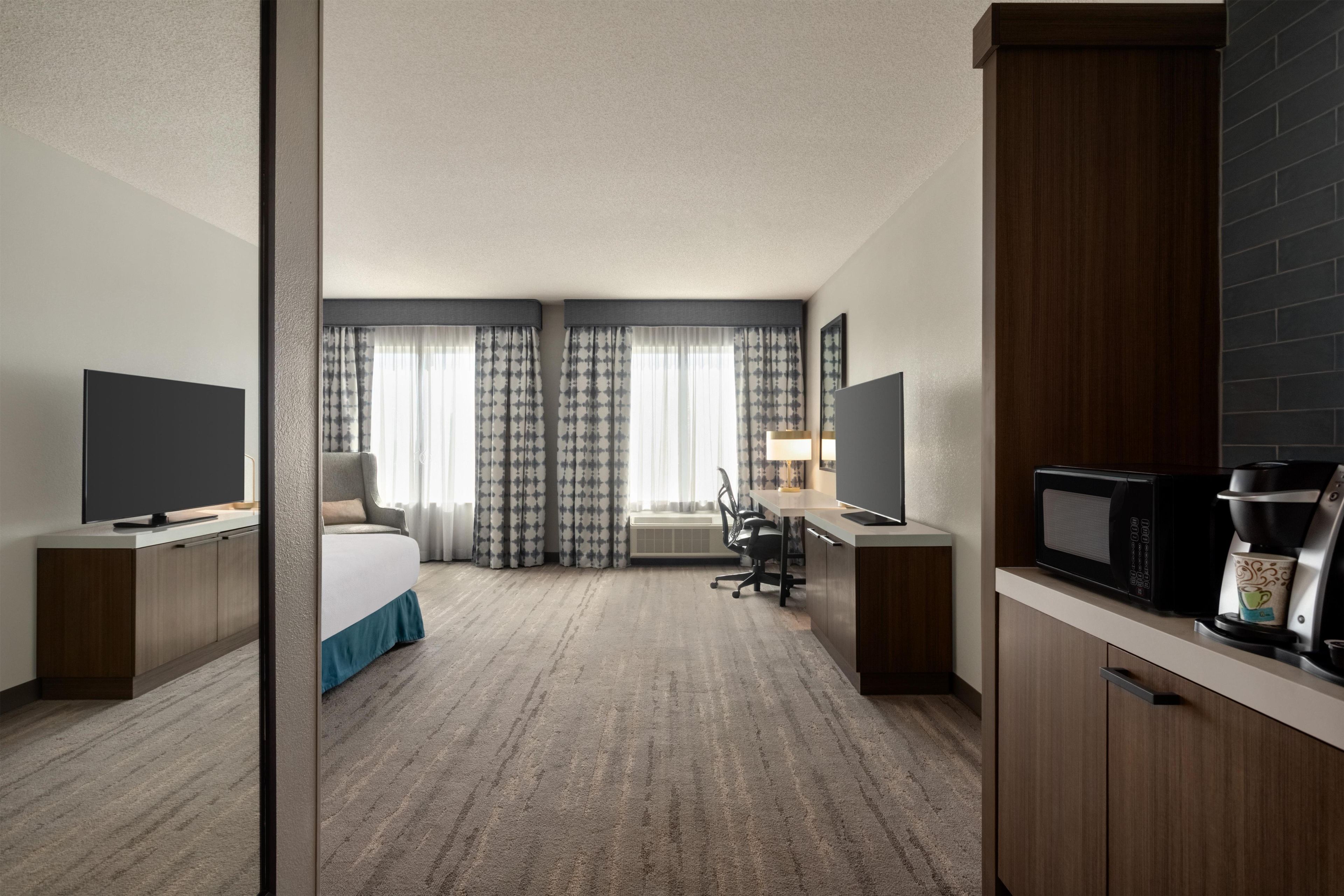 Habitación de hotel con cama, escritorio, televisor, cafetera y vista al exterior.