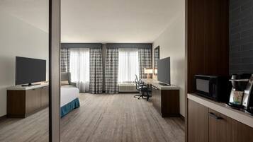 Habitación de hotel con cama, escritorio, televisor, cafetera y vista al exterior.