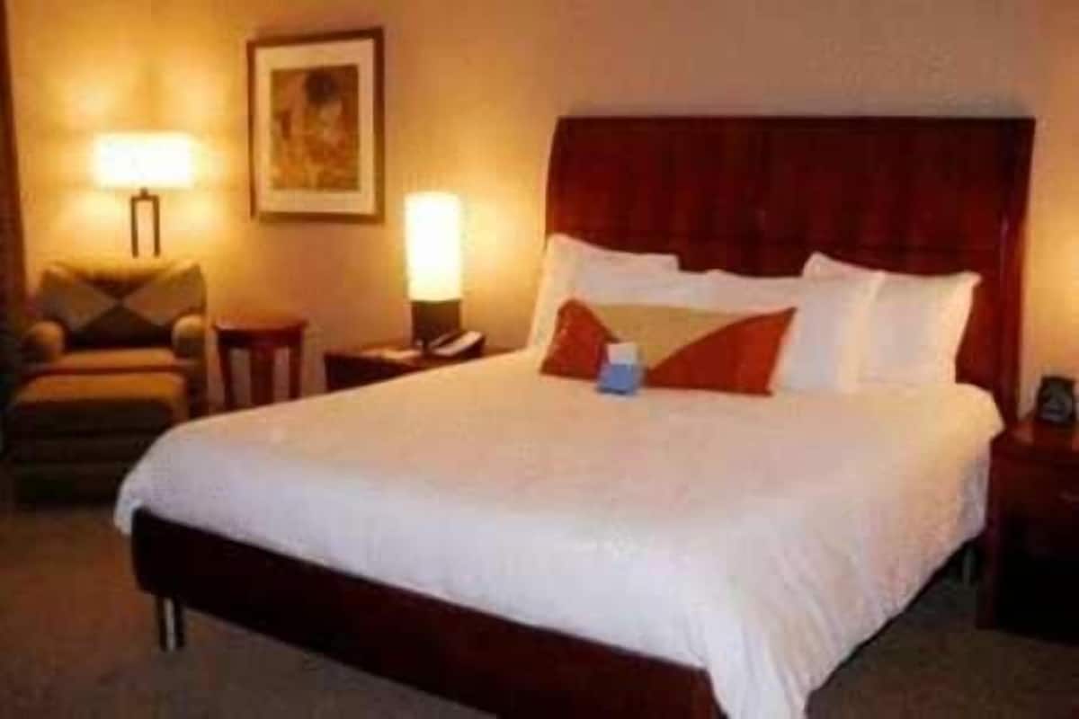 Ein Hotelzimmer mit einem großen Bett, zwei Nachttischen, einem Sessel und einer Wandlampe.