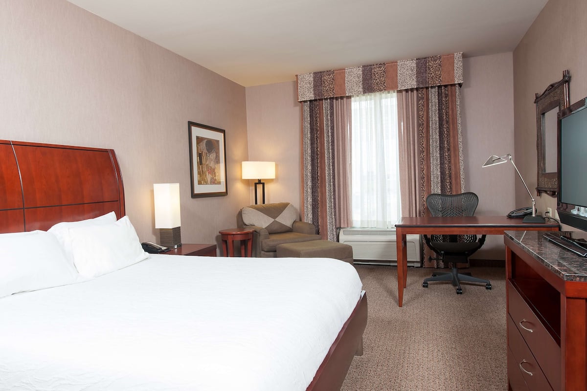 Ein Hotelzimmer mit einem großen Bett, einem Schreibtisch, einem Sessel, einer Lampe und einem Fernseher.