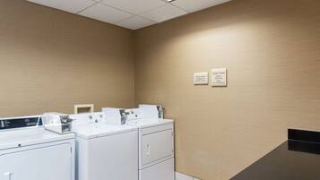 A laundry room with two washing machines and dryers, a sink, and a sign indicating the cycle times for each machine.