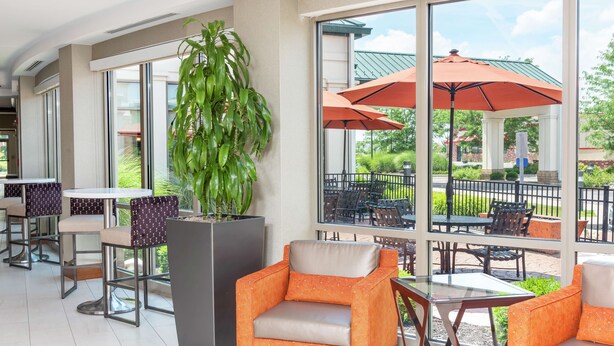 A sunlit indoor patio with orange chairs and tables, large windows, and a potted plant.