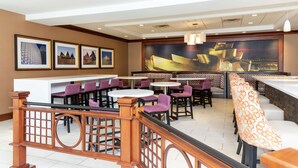 A restaurant with round tables and purple chairs, a wooden railing, and framed pictures on the wall.