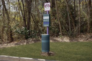 A dog waste station with a sign and a trash bin in a wooded area. - Homewood Suites by Hilton Birmingham-SW-Riverchase-Galleria (Birmingham)