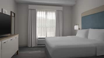 A hotel room with a bed, a TV on a wooden dresser, a window with curtains, and a bedside lamp.