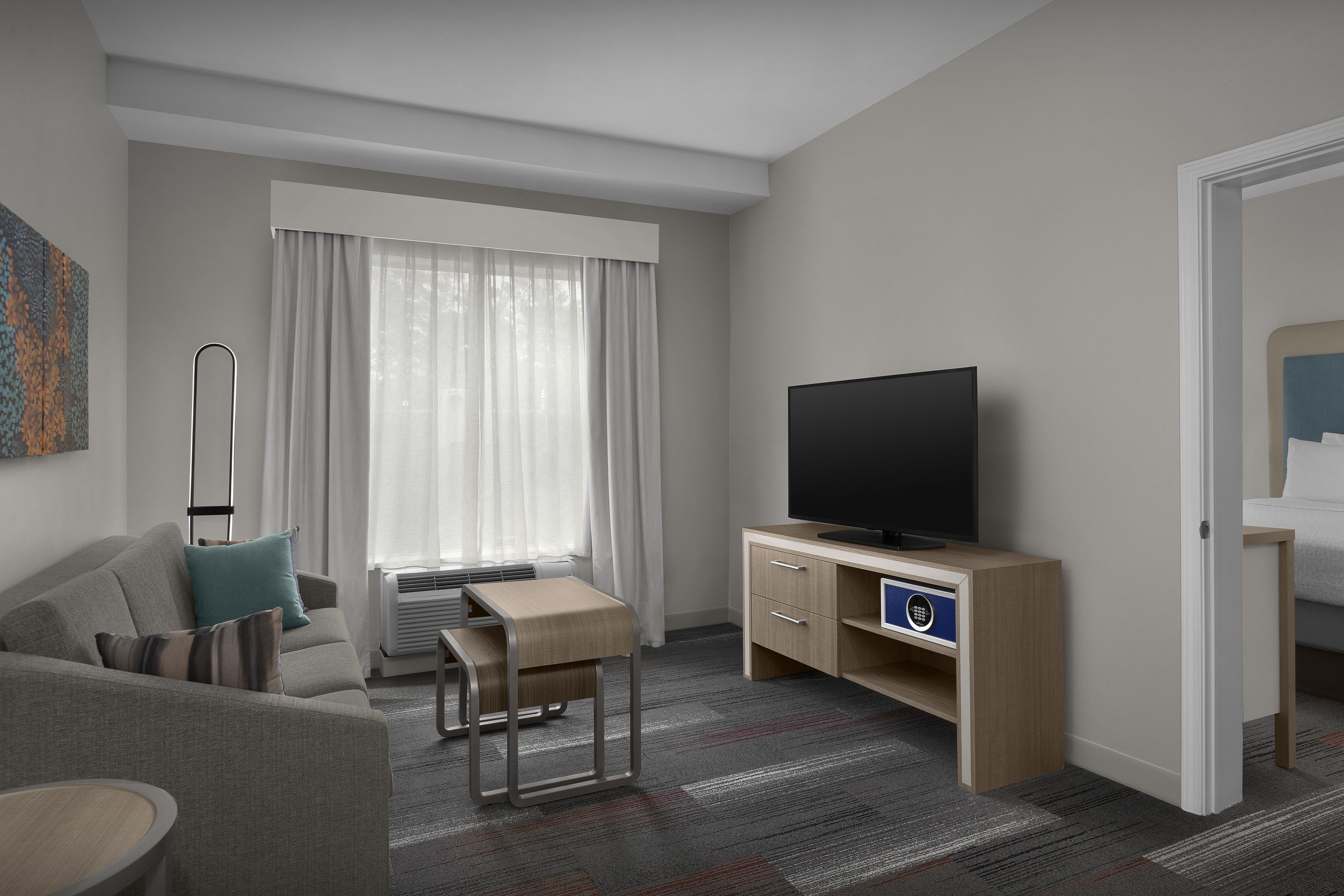 Et hotelværelse med sofa, lille bord, fjernsyn på et træstel og seng med sengegavl.