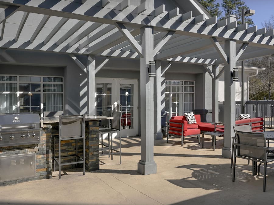 An outdoor patio area with a grill, seating, and a pergola structure.