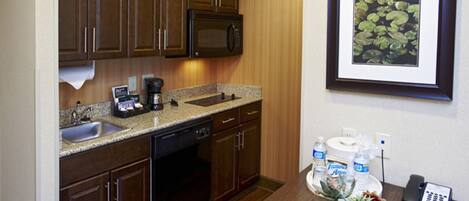 A kitchen with dark wooden cabinets, a granite countertop, a microwave, and a coffee maker. There is a framed picture of water lilies on the wall.