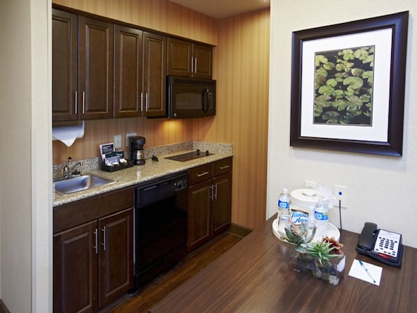 A kitchen with dark wooden cabinets, a granite countertop, a microwave, and a coffee maker. There is a framed picture of water lilies on the wall.