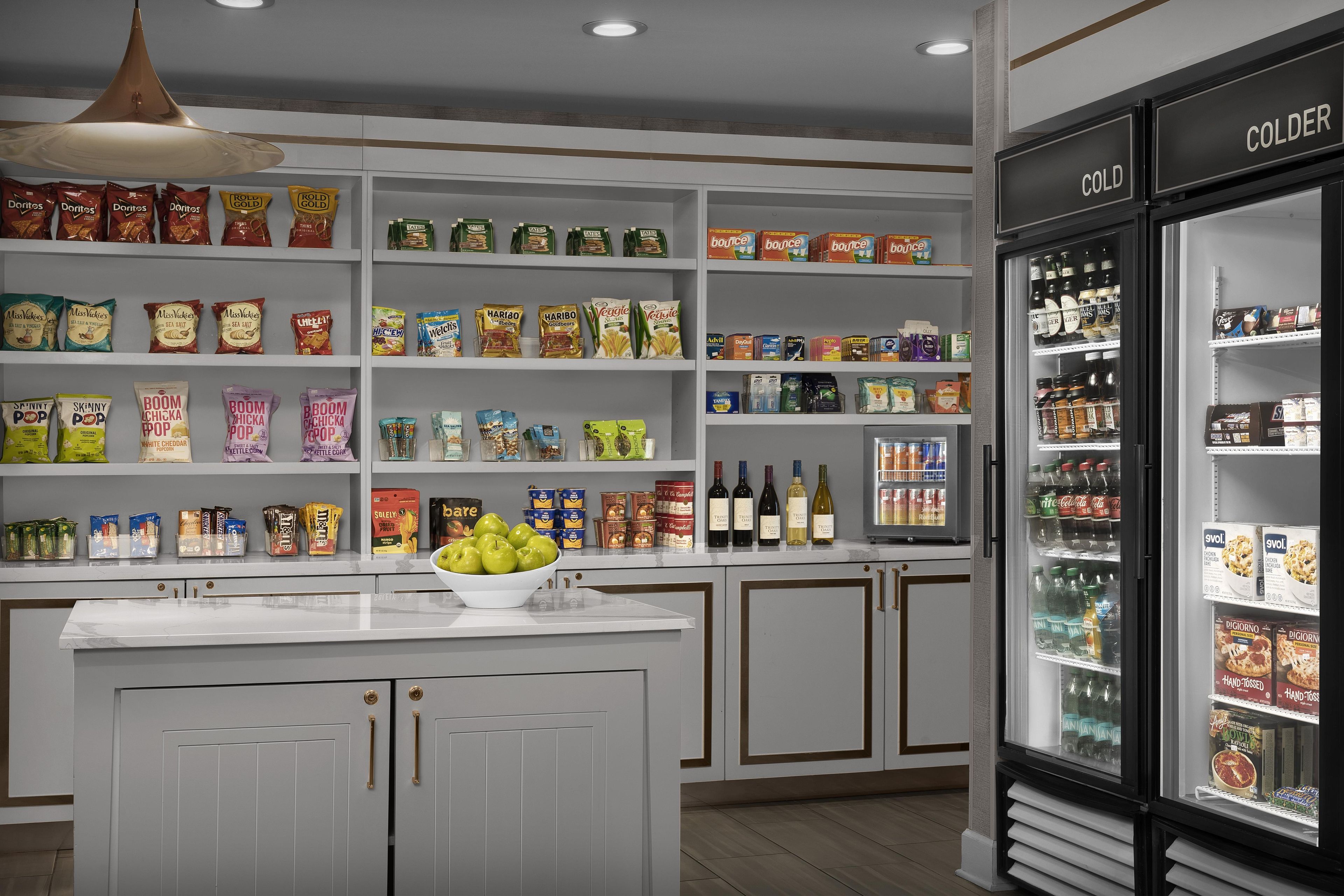 Interno di un negozio di alimentari con scaffali pieni di snack, bevande e un reparto refrigerato.