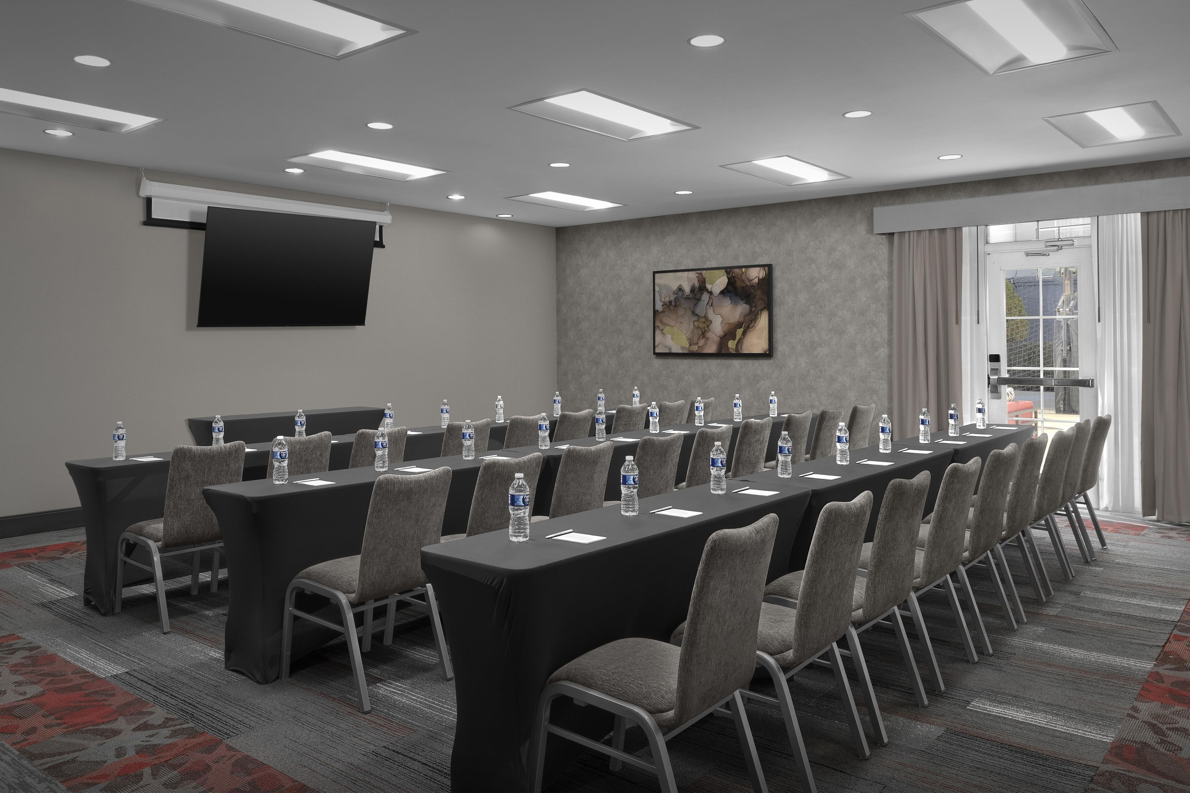 A conference room with a long table, chairs, water bottles, and a projector screen.