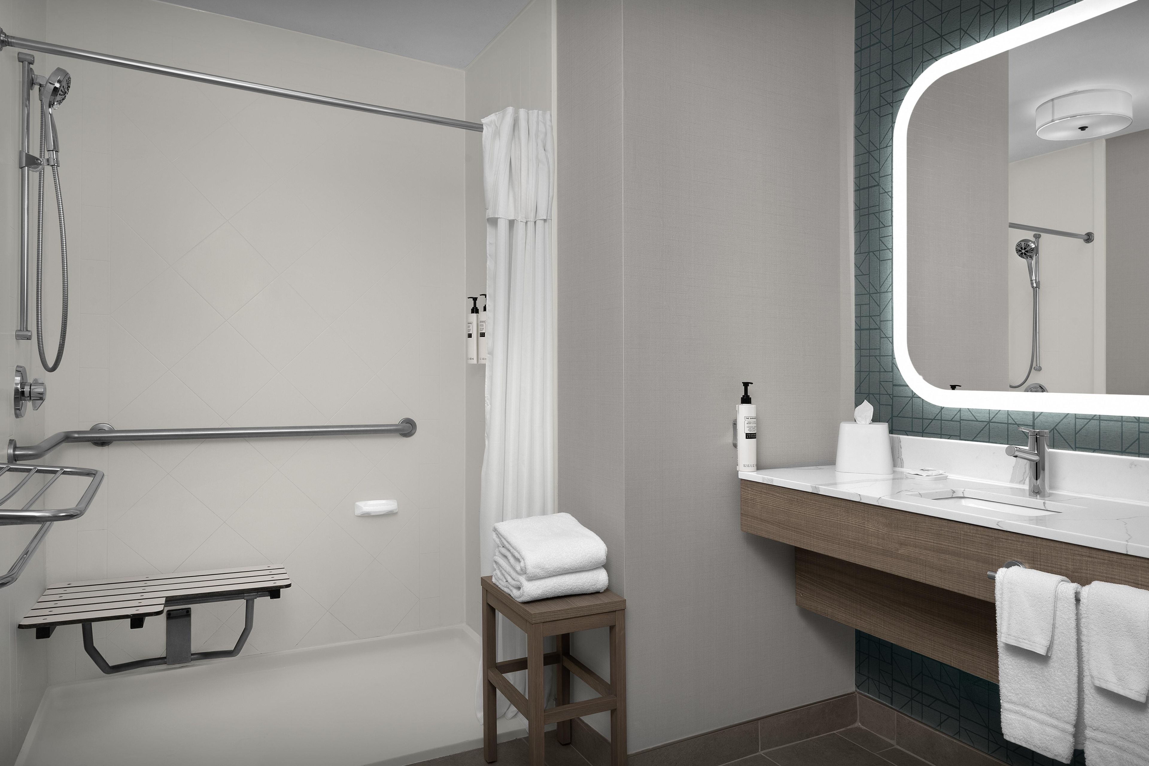 A modern bathroom with a shower, grab bar, towel rack, and a vanity with a mirror.
