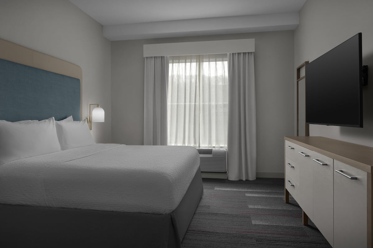 A hotel room with a bed, a TV, a desk, and a window with curtains.
