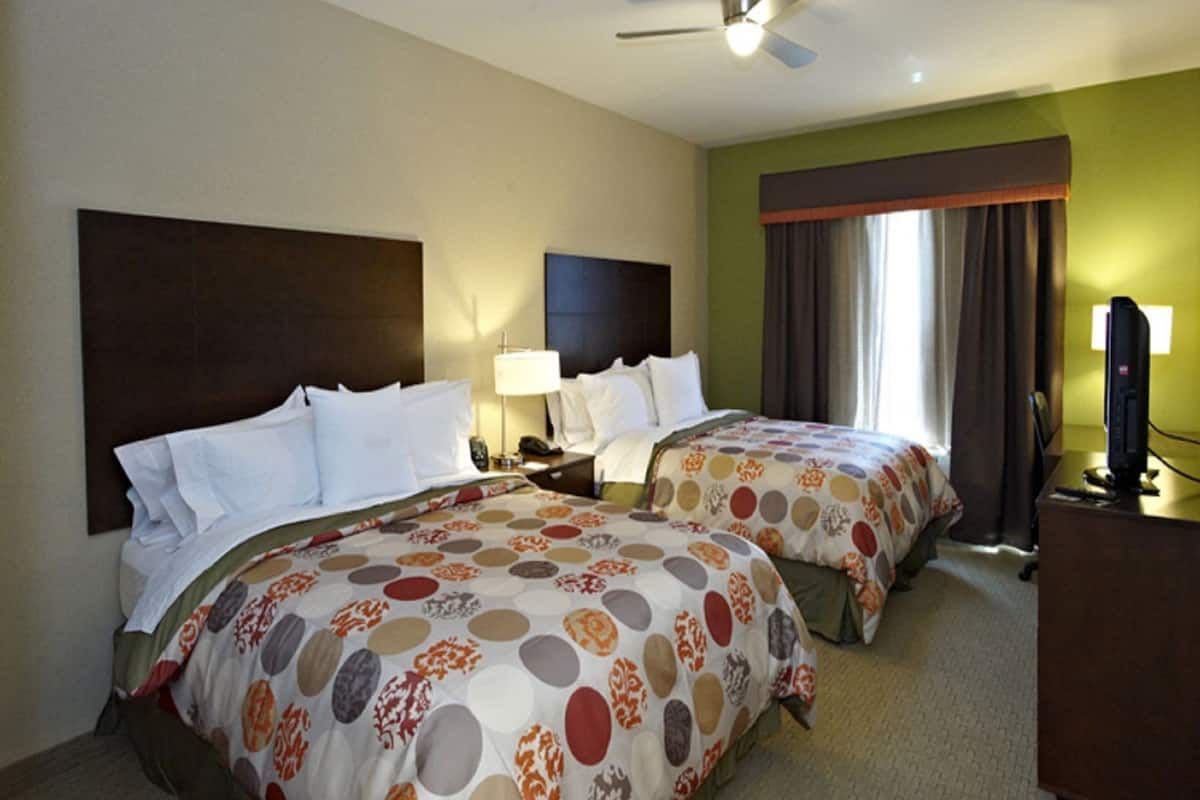 A hotel room with two beds, a ceiling fan, a television, and a window with curtains.