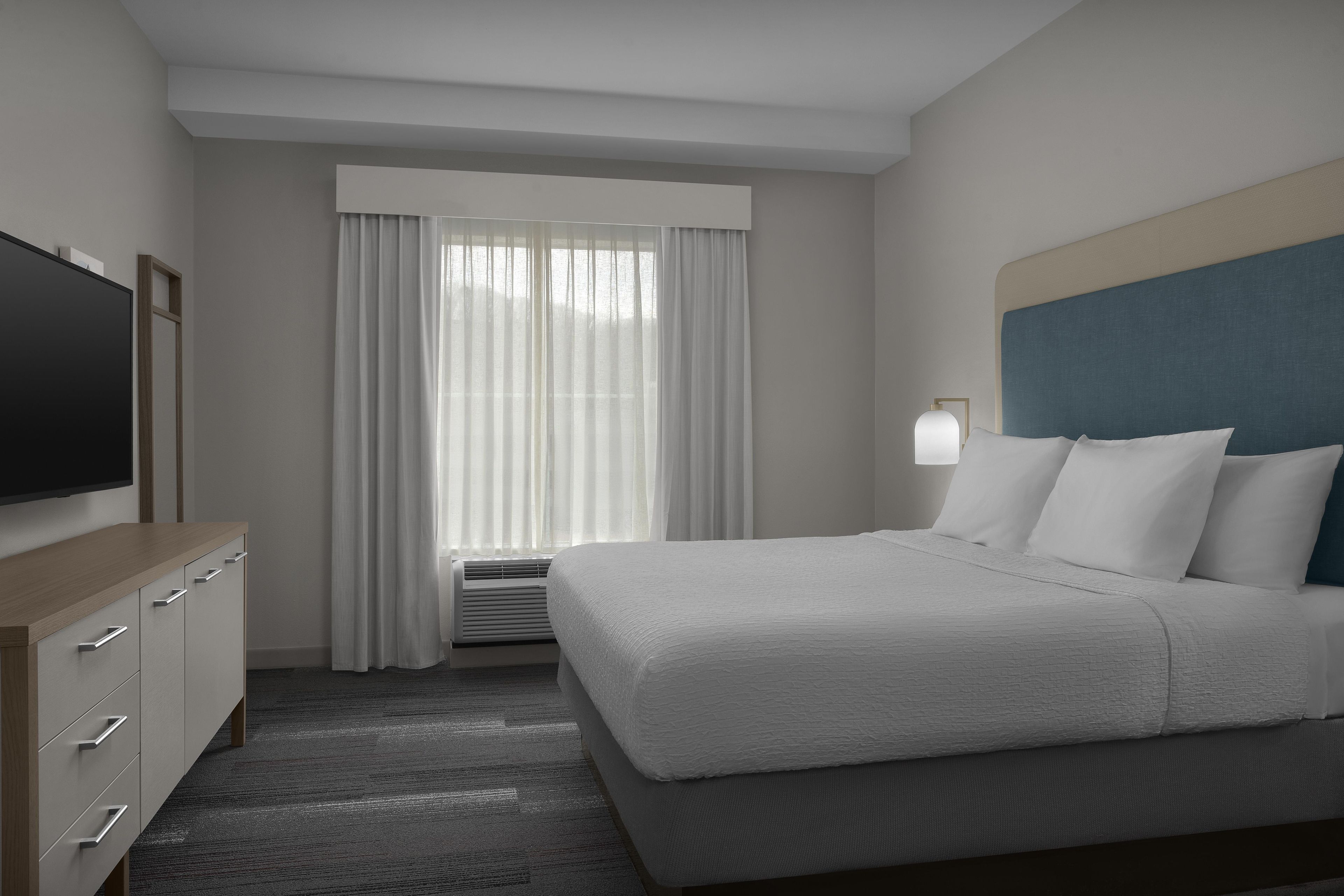 A hotel room with a bed, a television, a desk, and a window with curtains.