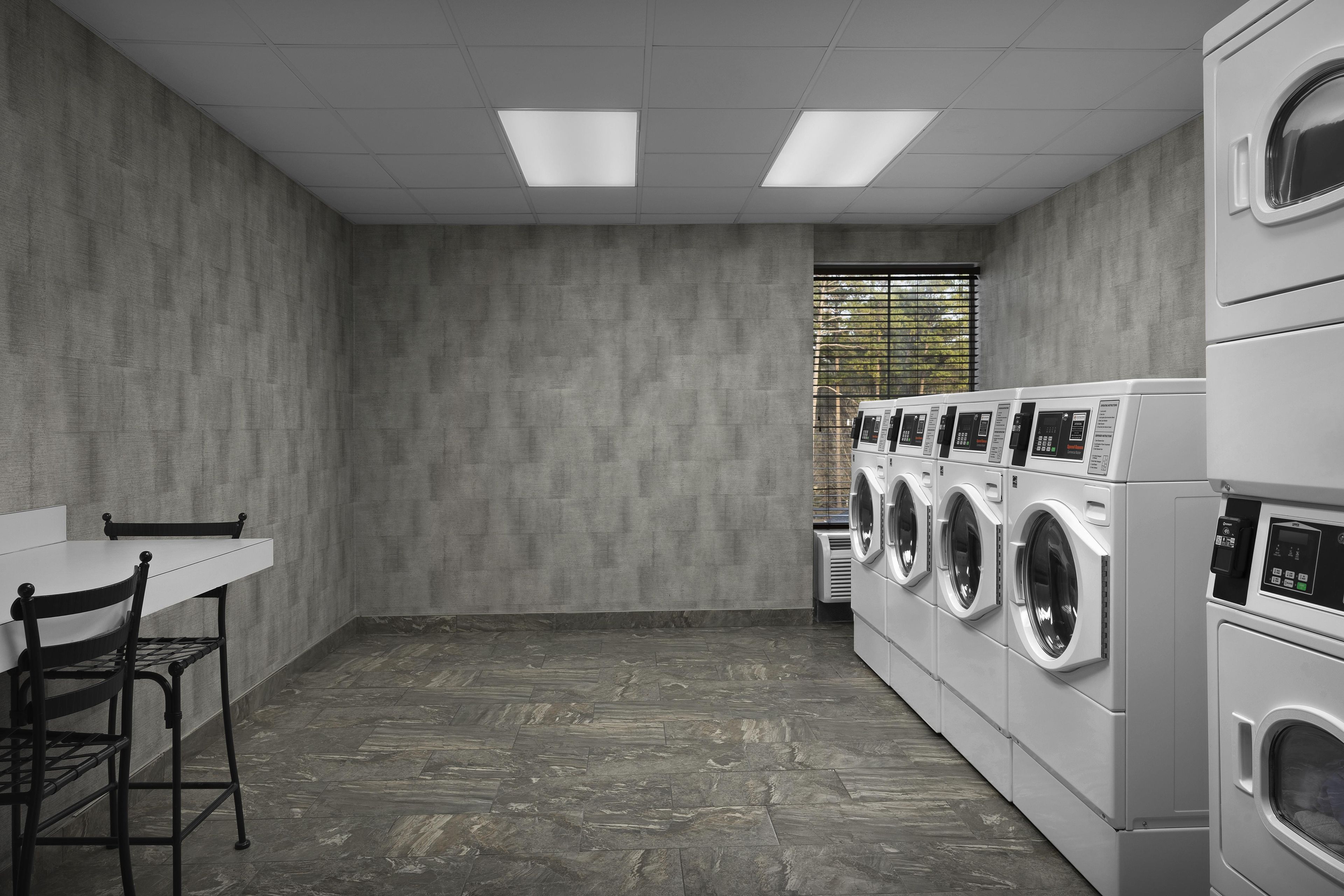 A laundry room with a table, chairs, and a row of stacked washing machines.