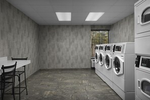 A laundry room with a table, chairs, and a row of stacked washing machines.