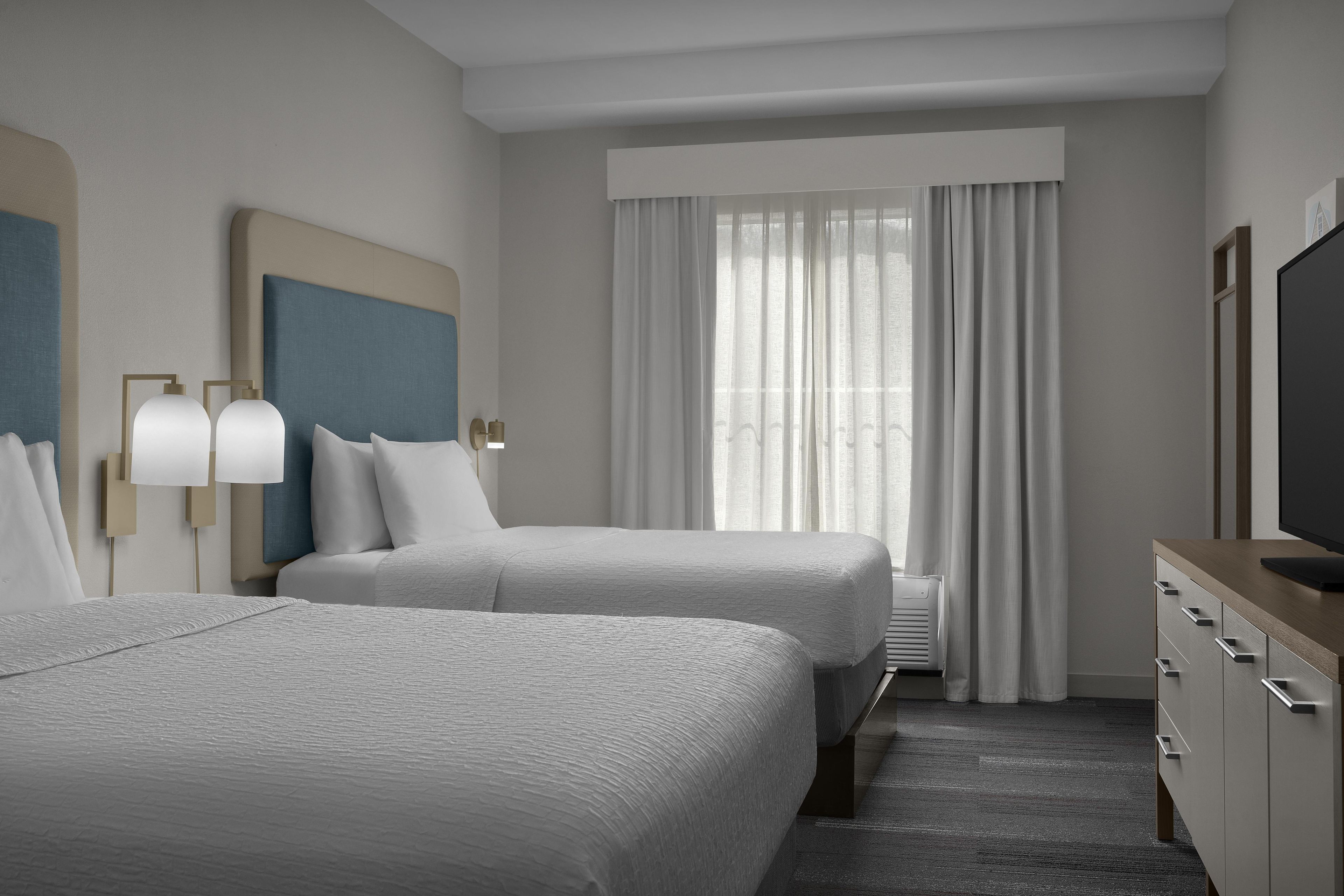 A hotel room with two beds, a large window with curtains, a flat-screen TV, and a minibar.