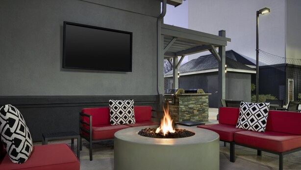 A circular fire pit with red seating and black-and-white patterned cushions, a flat-screen TV mounted on a wall, and a stone feature in the background.