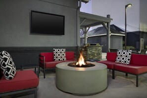 A circular fire pit with red seating and black-and-white patterned cushions, a flat-screen TV mounted on a wall, and a stone feature in the background. - Homewood Suites by Hilton Birmingham-SW-Riverchase-Galleria (Birmingham)