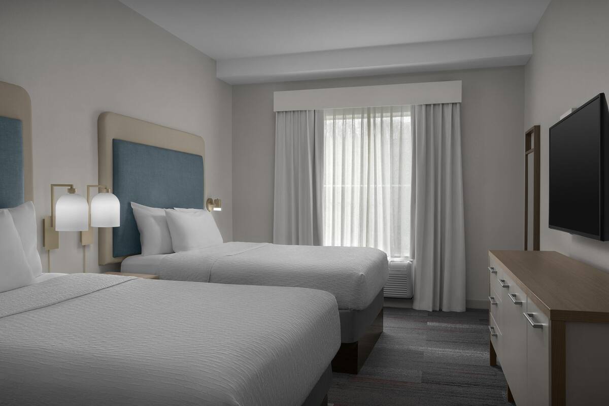 A hotel room with two beds, a TV, a dresser, and a window with curtains.