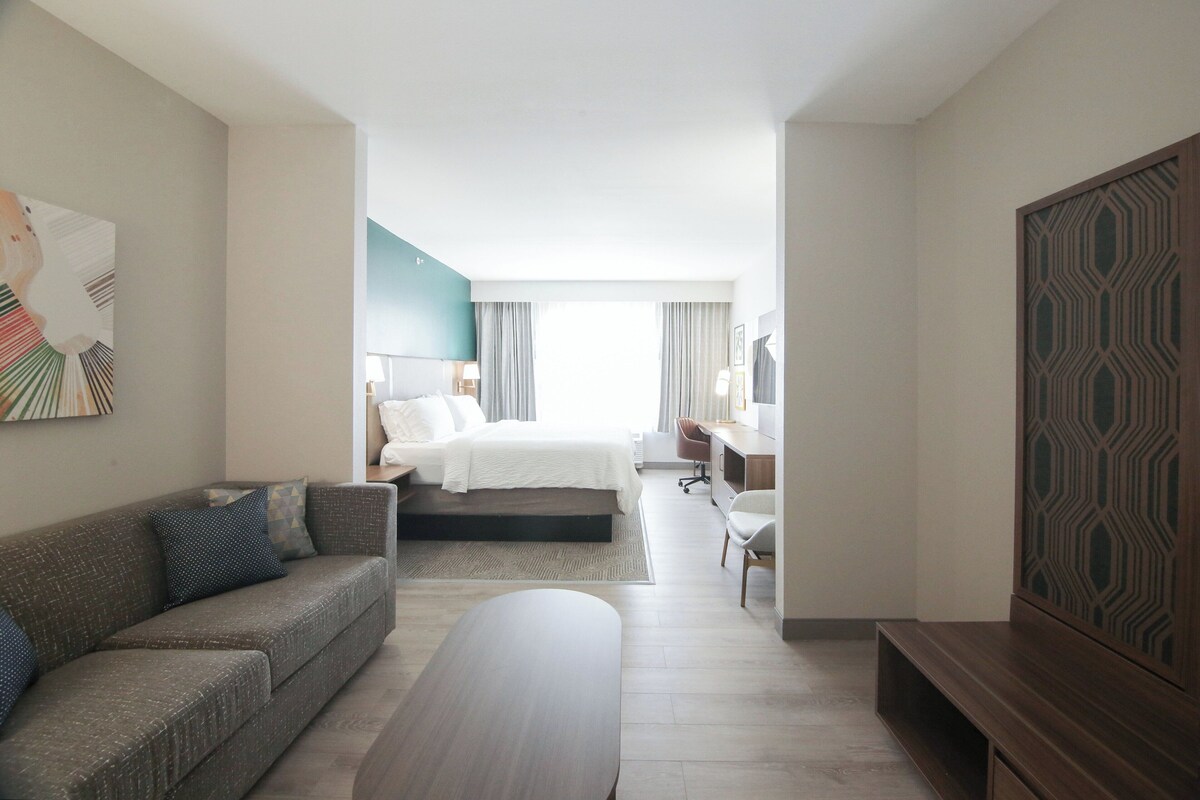A modern hotel room with a bed, a sofa, a desk, and a TV.