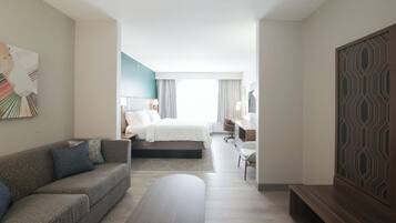 A modern hotel room with a bed, a sofa, a desk, and a TV.