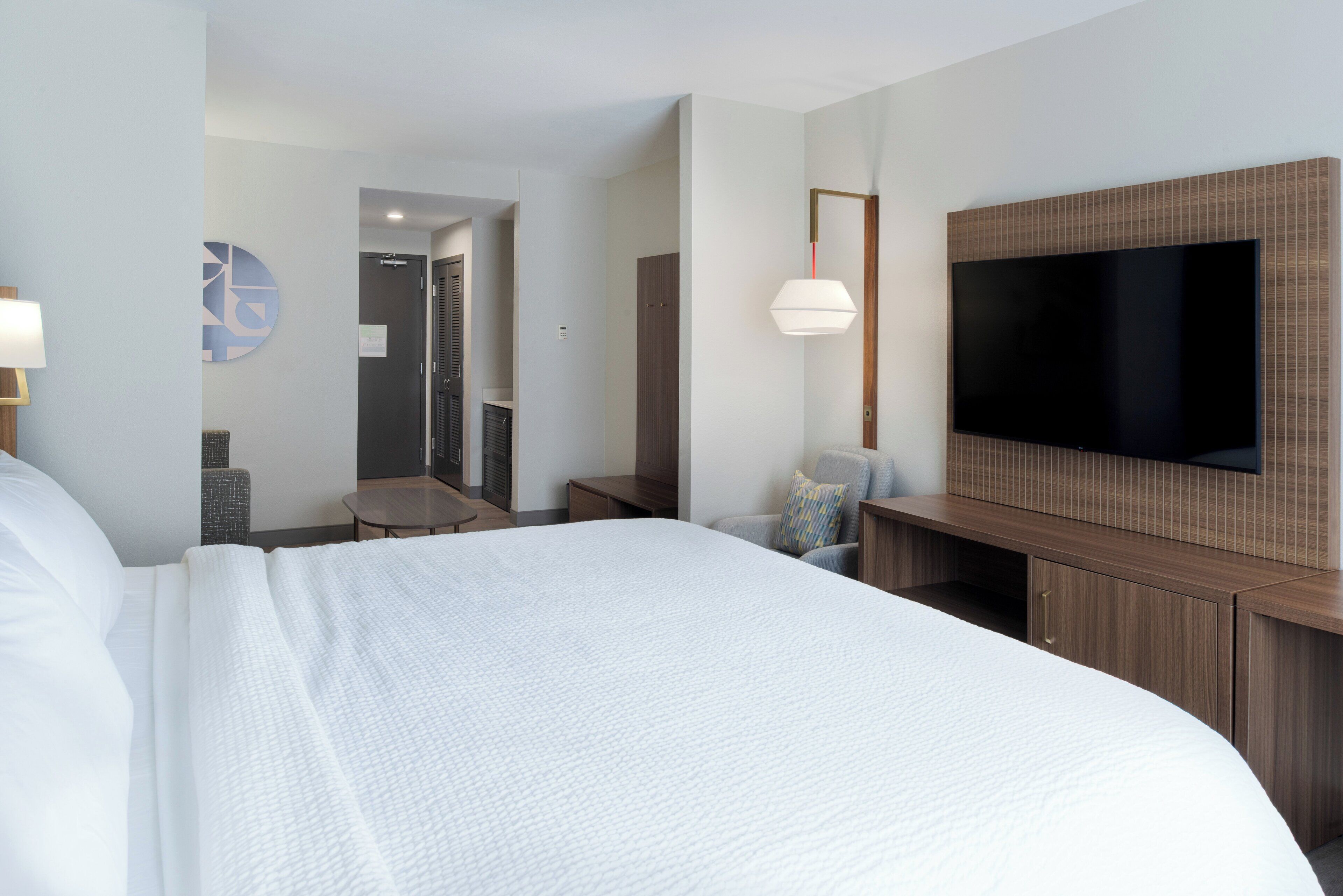 Habitación de hotel con una cama grande, un televisor montado en la pared, un escritorio y una silla.