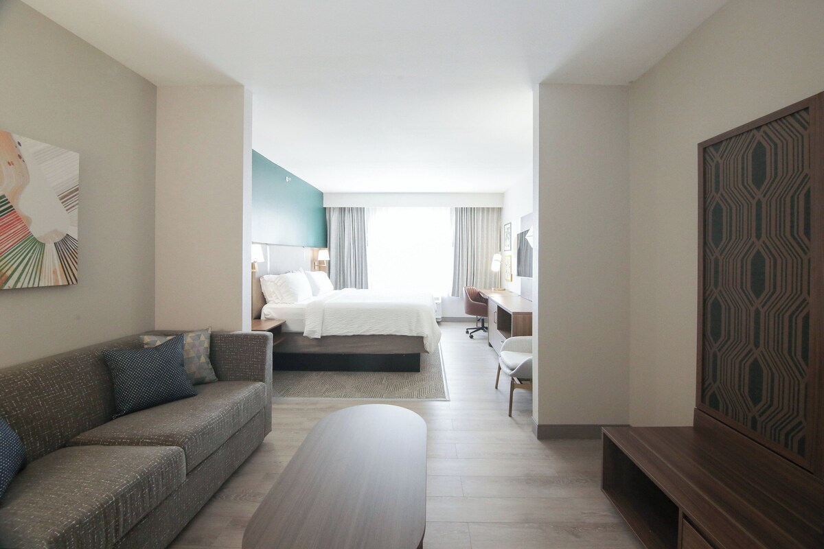 A modern hotel room with a bed, a sofa, a desk, and a TV.