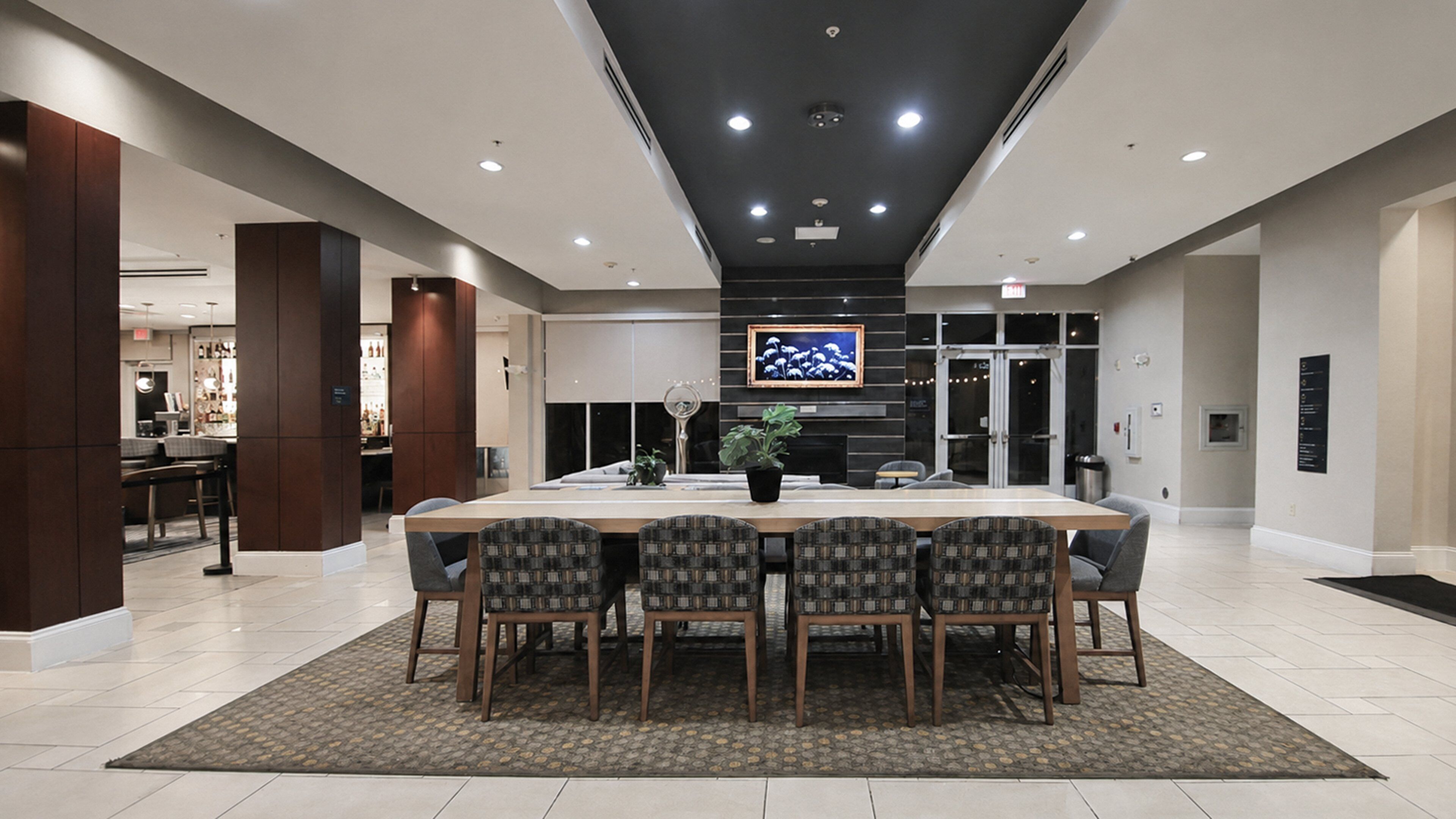 A spacious dining area with a long table and chairs, a potted plant, and a television mounted on the wall.