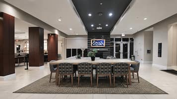 A spacious dining area with a long table and chairs, a potted plant, and a television mounted on the wall.
