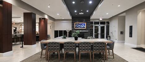 A spacious dining area with a long table and chairs, a potted plant, and a television mounted on the wall.