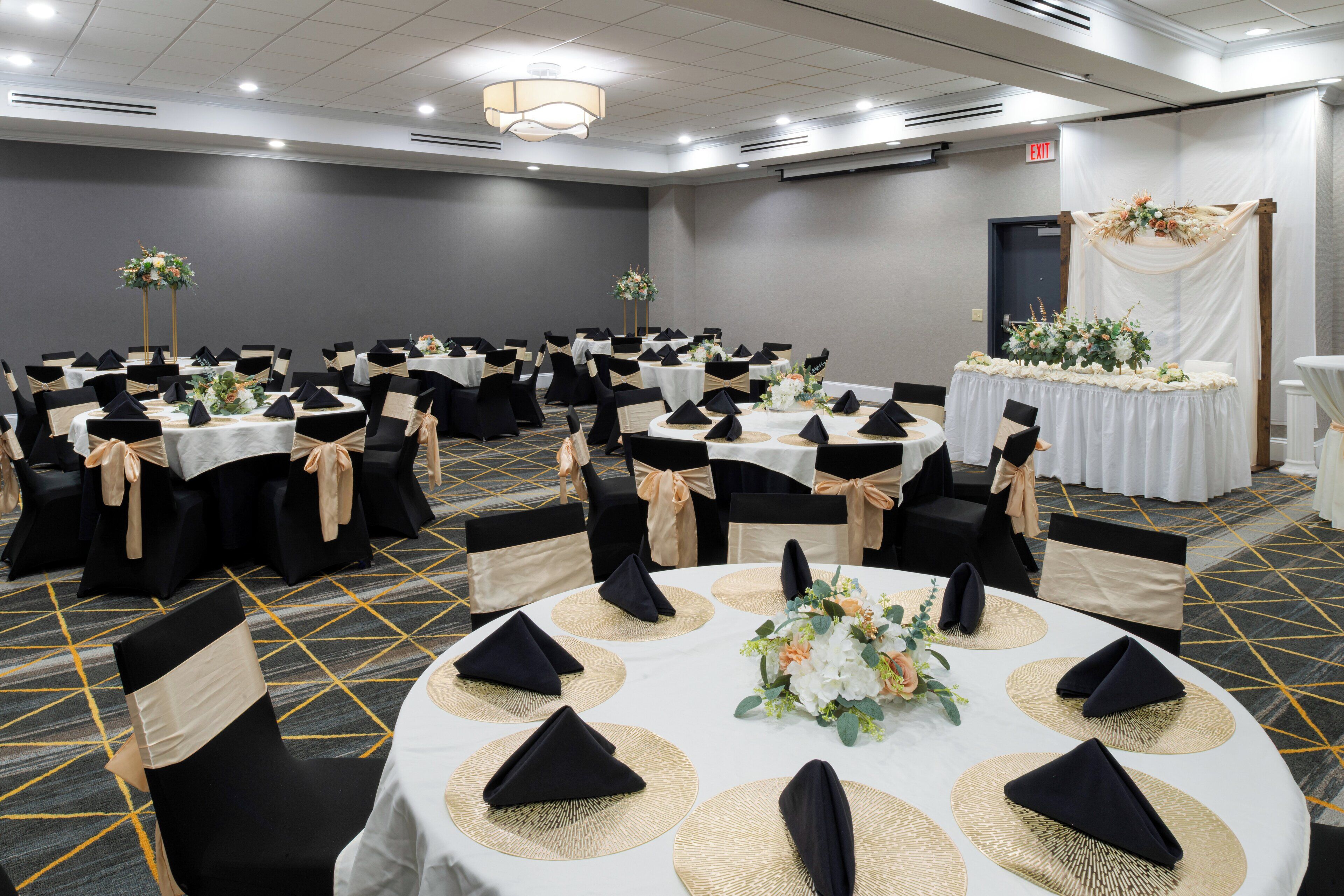 A conference room with round tables, black chairs, and beige sashes. Tables are set with white tablecloths, black napkins, and centerpieces.